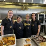 Four volunteers standing behind prepared meals at Soul Hub's community kitchen in Newcastle.